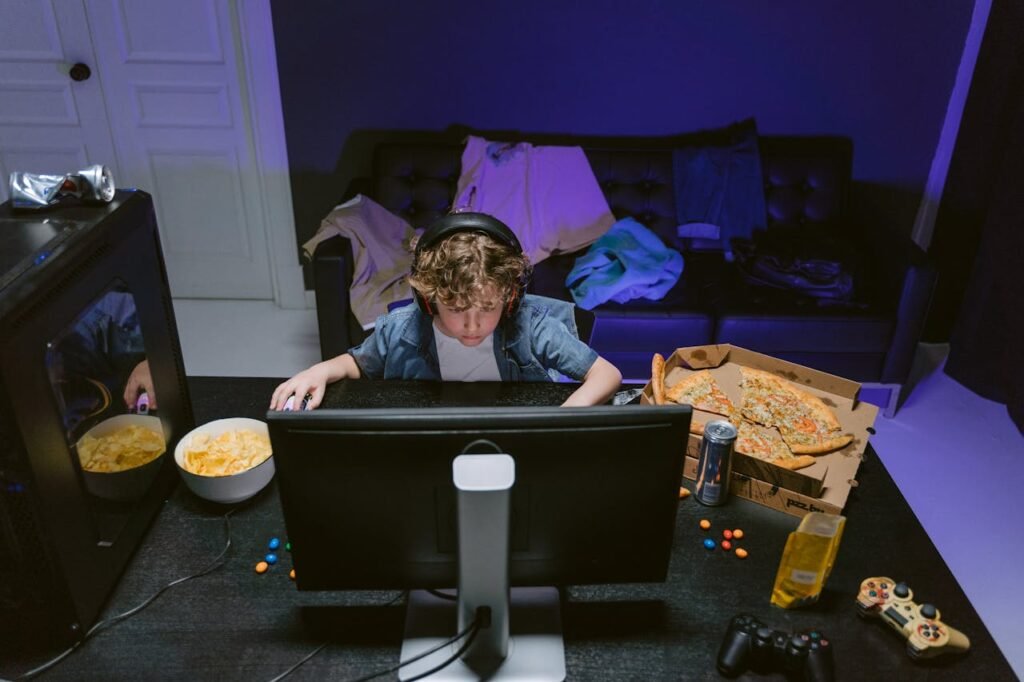 A Boy Wearing a Headset Using a Computer on Table with Food